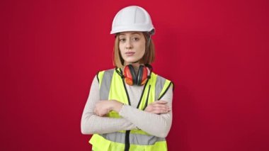 Sarışın, genç bir mimar. Kendine güvenen, kollarını kavuşturmuş kırmızı arka planda duran.