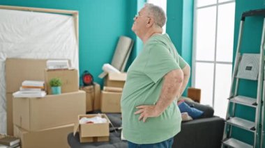 Orta yaşlı, kır saçlı bir adam geriye doğru duruyor ve yeni evine bakıyor.