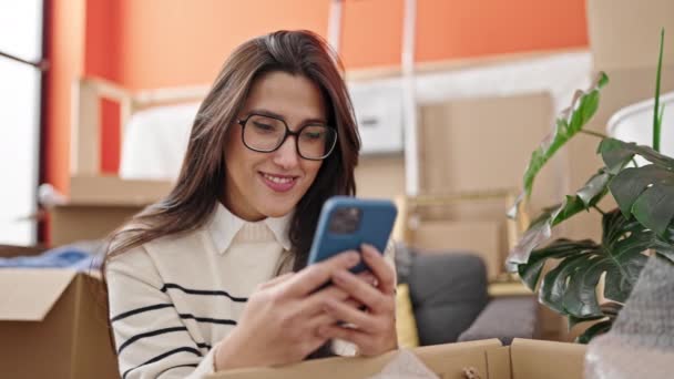 年轻美丽的惊慌失措的女人在新家用智能手机打开纸板箱 — 图库视频影像