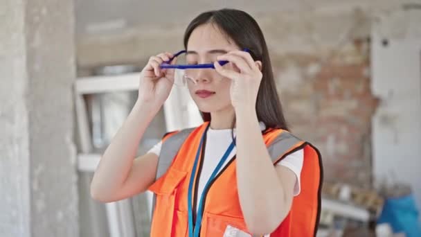 若いです中国の女性ビルダー身に着けていますセキュリティ眼鏡行います親指アップジェスチャーで建設現場 — ストック動画