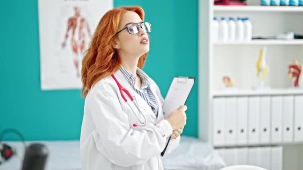 红头发的年轻女医生拿着剪贴板在诊所微笑 — 图库视频影像