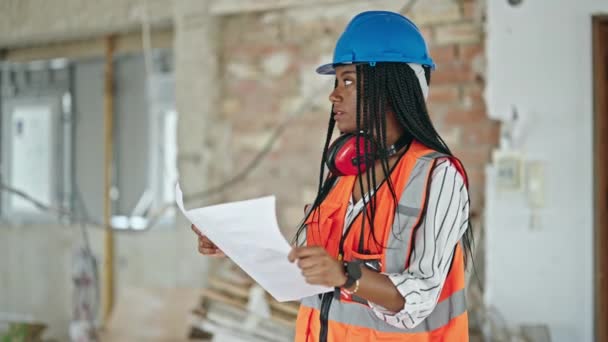 アフリカ系アメリカ人の女性建築家が建設現場でリラックスした表情読み取りハウスプロジェクトで立っている — ストック動画