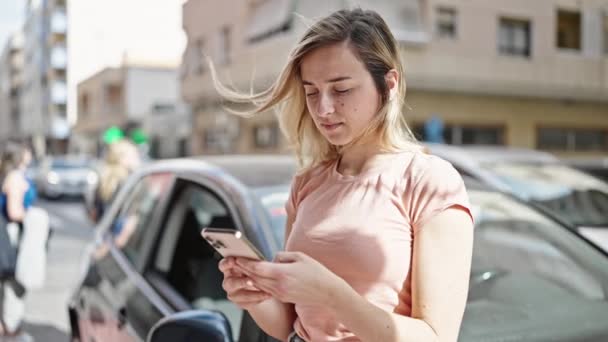 Νεαρή Ξανθιά Γυναίκα Που Χρησιμοποιεί Smartphone Στέκεται Αυτοκίνητο Στο Δρόμο — Αρχείο Βίντεο