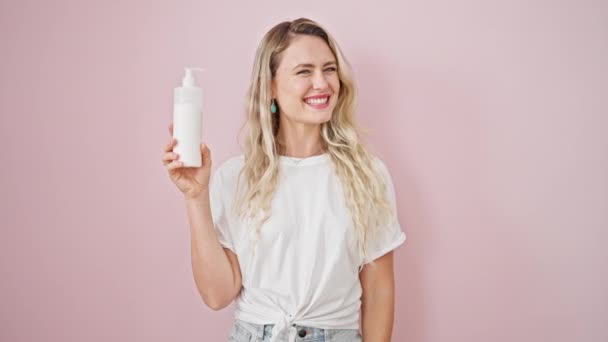 Joven Mujer Rubia Sonriendo Confiada Sosteniendo Botella Crema Sobre Fondo — Vídeos de Stock