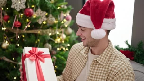 Mladý Hispánec Muž Usměvavý Nosí Vánoční Klobouk Poslech Uvnitř Dárek — Stock video