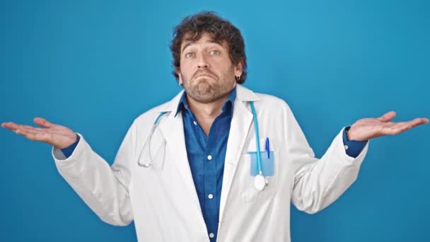 Junger Hispanischer Arzt Steht Ratlos Vor Isoliertem Blauen Hintergrund — Stockvideo