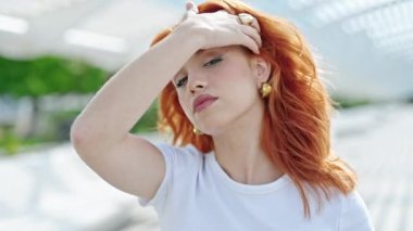 Genç kızıl saçlı kadın, rahatlamış bir ifadeyle parkta elleriyle saçlarını tarıyor.