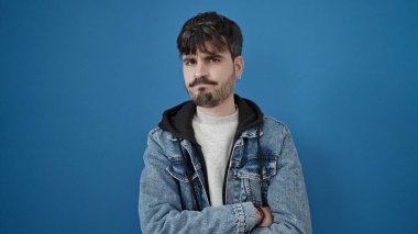 İzole edilmiş mavi arka planda üzgün bir ifadeyle duran İspanyol genç adam.
