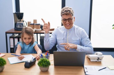 Ofiste birlikte çalışan genç baba ve kız mutlu bir şekilde el ve parmak kenarı işaret ediyor. 