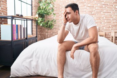 Genç İspanyol adam yatakta otururken stresli.