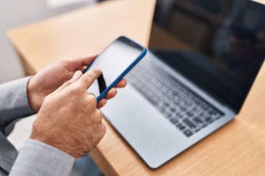 Ofiste akıllı telefon ve dizüstü bilgisayar kullanan genç bir İspanyol.