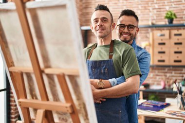 İki erkek sanatçı birbirlerine sarılıp resim stüdyosunda resim çekiyorlar.