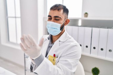 Tıbbi maske takan genç İspanyol doktor klinikte eldiven takıyor.