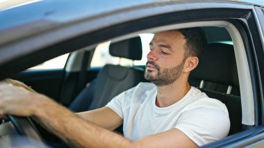 Young hispanic man smiling confident driving car at street