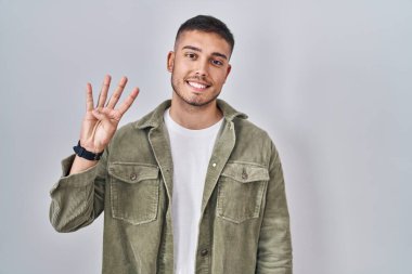 Tecrit edilmiş arka planda duran genç İspanyol adam, dört numarayı gösterip işaret ederken kendinden emin ve mutlu gülümsüyor.. 