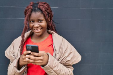 Siyah arka planda akıllı telefon kullanarak gülümseyen Afrikalı Amerikalı kadın.