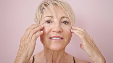 Orta yaşlı sarışın kadın, pembe arka planda kendine güvenen, güler yüzlü bir kadın.