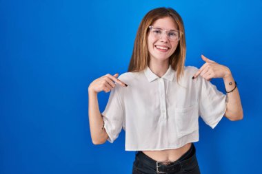 Güzel bir kadın mavi arka planda duruyor. Kendine güveni tam görünüyor. Kendini gururlu ve mutlu bir şekilde gösteriyor.. 