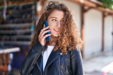 Genç, güzel, İspanyol bir kadın gülümsüyor ve markette akıllı telefondan konuşuyor.