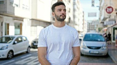 Latin kökenli genç adam ciddi bir ifadeyle sokağa bakıyor.