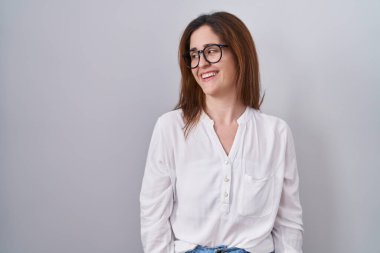 Esmer kadın, izole edilmiş beyaz arka planda duruyor. Yüzünde gülümseme, doğal bir ifade ile yan yana bakıyor. Kendinden emin gülen. 