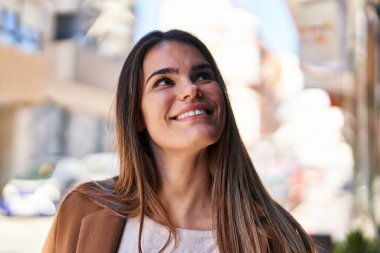 Young beautiful hispanic woman smiling confident looking to the sky at street