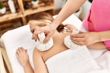 Masaya uzanmış beyaz bir kadın güzellik salonundaki Tayland çantalarıyla sırt masajı yaptırıyor.