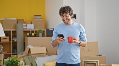 Genç İspanyol adam akıllı telefon kullanıyor. Yeni evinde kahve içiyor.