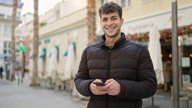 Kafe terasında gülümseyen akıllı telefon kullanan genç bir İspanyol.