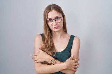 Beyaz arka planda duran beyaz tenli genç kadın yüzünde üzgün bir ifadeyle kış soğuğundan titriyor ve donuyor. 