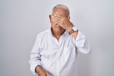 Senior man with grey hair standing over isolated background covering eyes with hand, looking serious and sad. sightless, hiding and rejection concept 