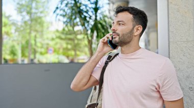 Genç İspanyol adam akıllı telefondan konuşuyor. Sokakta sırt çantası takıyor.
