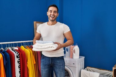 Çamaşır odasında katlanmış temiz havluları tutan genç İspanyol adam çılgınlığı kutluyor ve başarı için hayrete düşüyor.. 