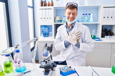 Bilim adamının laboratuvarında çalışan beyaz bir adam elleri göğsünde gülümsüyor, gözleri kapalı ve yüzünde minnet dolu bir jest var. sağlık kavramı. 