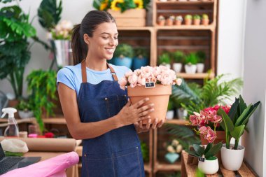 Young beautiful hispanic woman florist smiling confident holding plant at florist