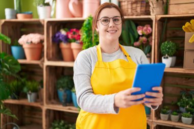 Young beautiful plus size woman florist smiling confident using touchpad at flower shop