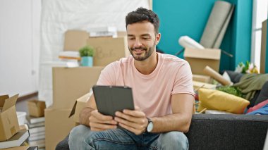 Yeni evindeki koltukta oturan dokunmatik ped kullanan İspanyol genç adam.