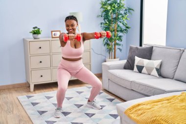 Afrika kökenli Amerikalı kadın evde dambıl kullanarak bacak egzersizi yapıyor.