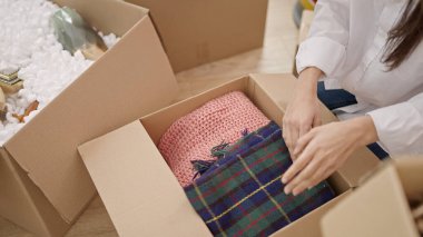 Young beautiful hispanic woman unpacking cardboard box at new home