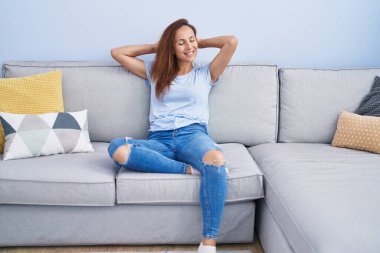 Young woman relaxed with hands on head sitting on sofa at home