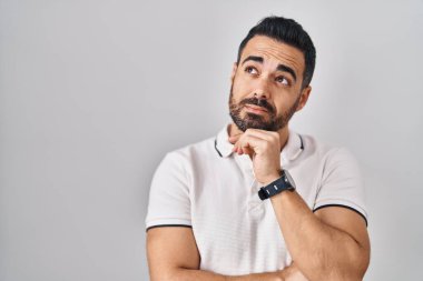 Beyaz arka plan üzerine gündelik kıyafetler giyen, eli çenesinde soru soran, düşünceli bir İspanyol genç adam. Düşünceli bir yüzle gülümsüyor. şüphe kavramı. 