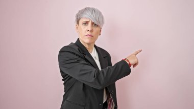Genç bir iş kadını, izole edilmiş pembe arka planda kızgın yüzüyle boş bir alanı işaret ediyor.
