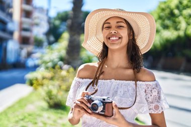 Genç Afrikalı Amerikalı kadın turist parkta kamerayla gülümsüyor.