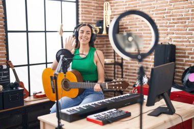 Young hispanic woman musician recording classical guitar lesson by the smartphone at music studio