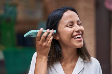 Young hispanic woman smiling confident listening audio message by the smartphone at street