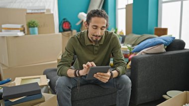 Yeni evindeki koltukta oturan dokunmatik ped kullanan İspanyol genç adam.