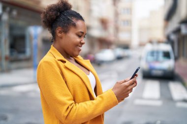 Afro-Amerikalı kadın sokakta akıllı telefon kullanarak kendine güveniyor.