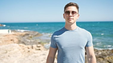 Deniz kenarında ciddi bir ifadeyle duran genç İspanyol turist.