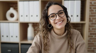 Genç, güzel, İspanyol bir iş kadını ofiste kendinden emin gülümsüyor.