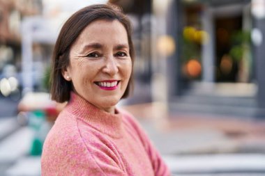 Orta yaşlı bir kadın sokakta kendine güvenerek gülümsüyor.